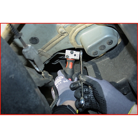 Hände mit Handschuhen verwenden Werkzeug, um etwas unter einem metallischen Fahrzeugteil zu bearbeiten.